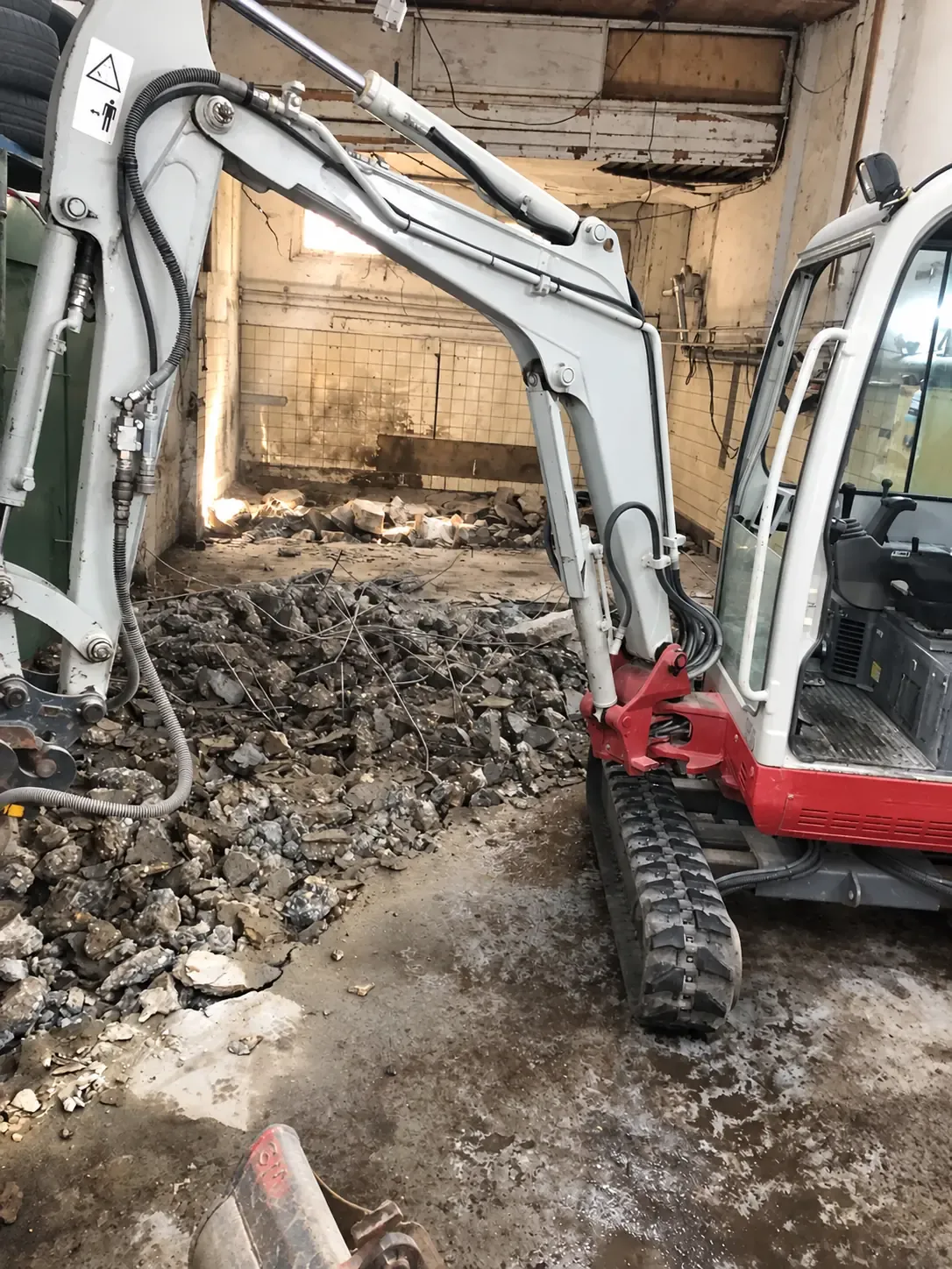 Een compacte graafmachine bij het verwijderen van een betonvloer.