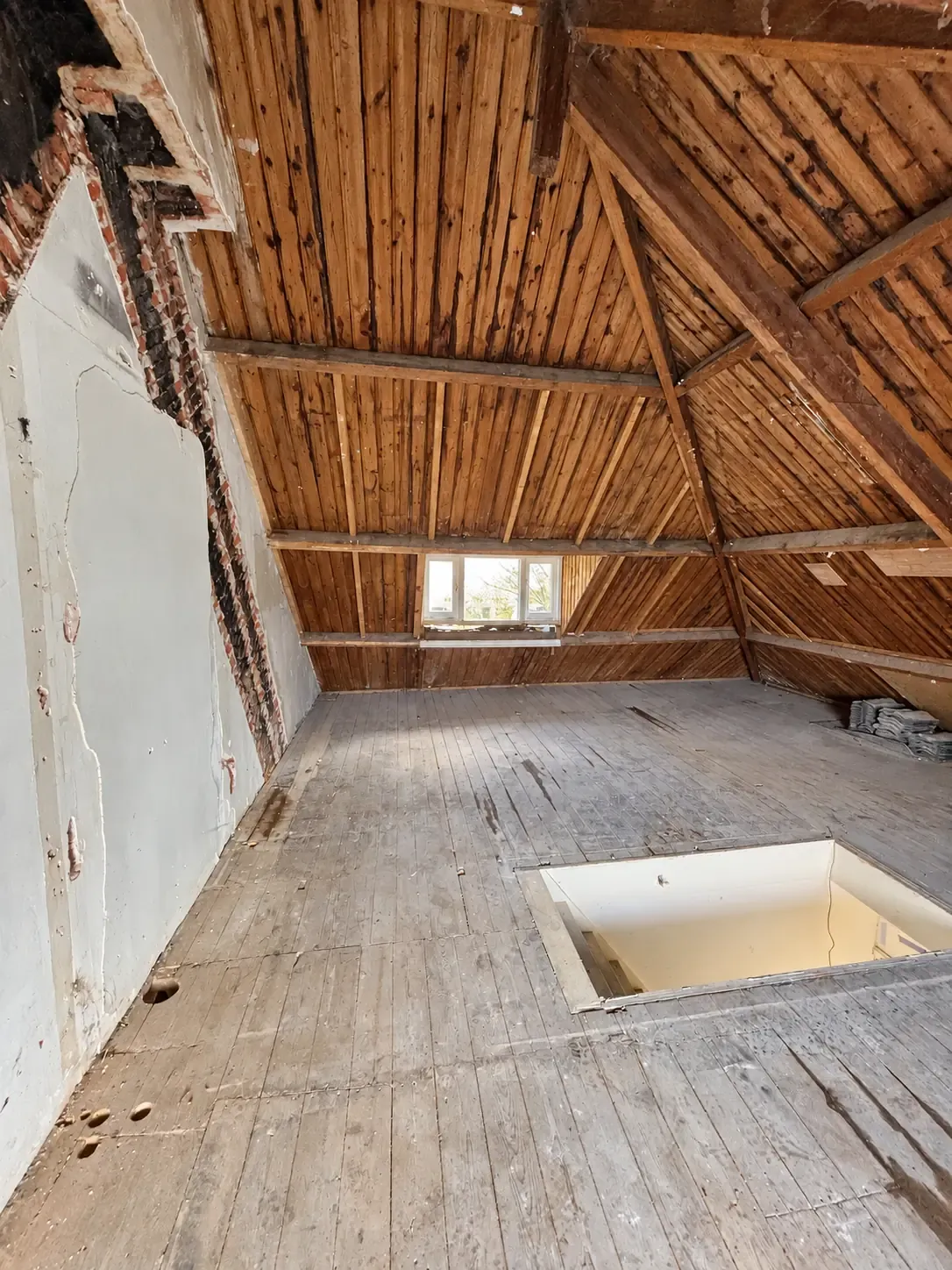 Een zolder met zichtbare houten dakconstructie en verwijderde afwerking.